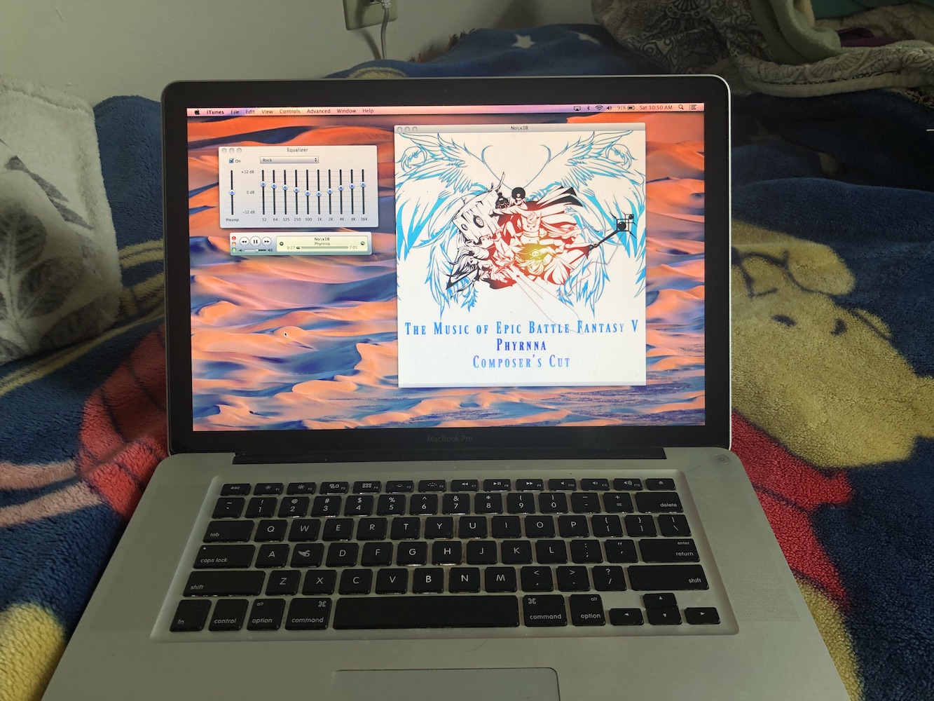 The 2011 MacBook Pro, running unplugged, with a default desert wallpaper, glossy menu bar, and a very old copy of iTunes, running in all its OS X 10.9 glory.