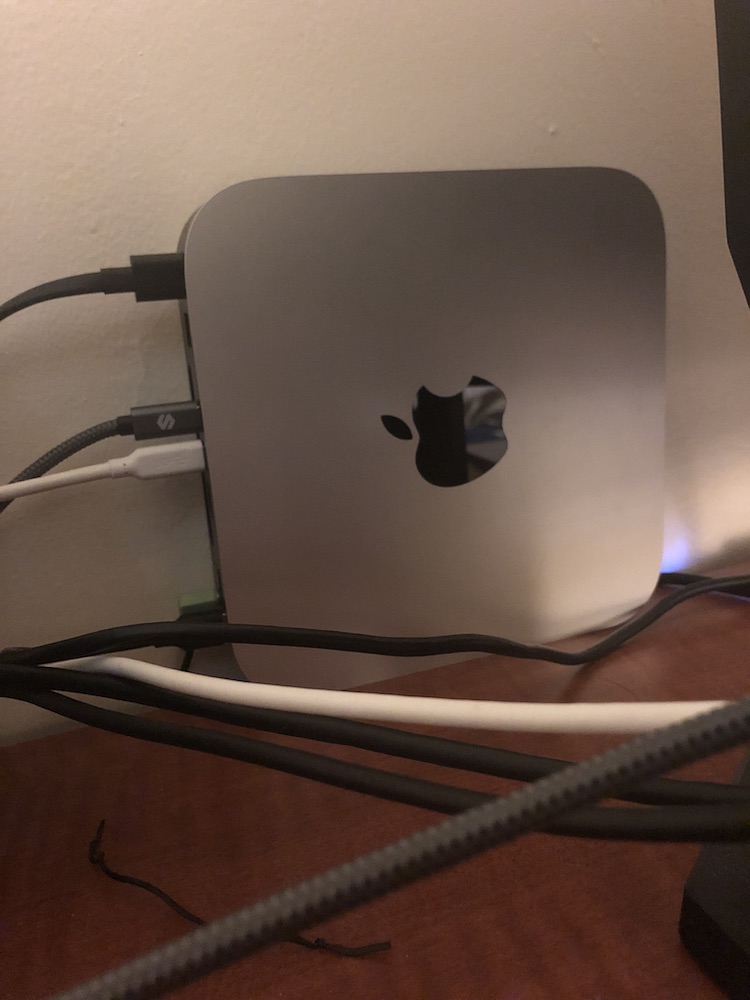 Mac Mini sat on its own left side so rear ports and cables go towards the room's left; the Apple logo is neither up nor down, with its bottom towards the room's right.