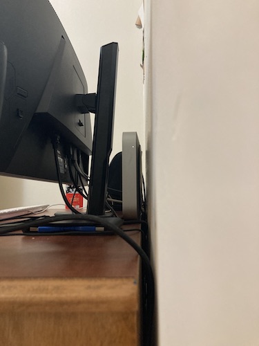 Shot of cable management from the opposite side at a lower angle, showing myriad wires plugged into the monitor's underside. The gap between the dresser and the wall is made clear by a close-up: it's only about one centimeter, much thinner than the depth of the standing Mac Mini.