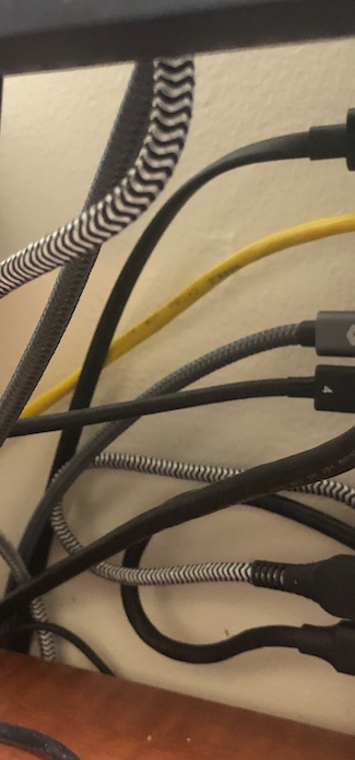 Close-up shot of the cables connected to the Mac in particular. From bottom to top: USB-A with a U-turn threading behind the Mac Mini and plugging into an external backup drive; USB-A with a thick, braided, zebra-colored wire curving extra length beneath the desk and snaking up to the monitor; symbol-marked Thunderbolt 4 USB-C coming forward and connecting to the USB dock; Silkland-branded USB-C also wrapping under the desk and eventually reaching the monitor; yellow ethernet cable going off into the distance, eventually reaching the Mac Pro; and power cable for the Mac Mini. A tiny aux jack is also plugged in near the bottom. The only free port is HDMI, which is lower-capability on the Mac Mini M1 model, so isn't ideal for a primary monitor.